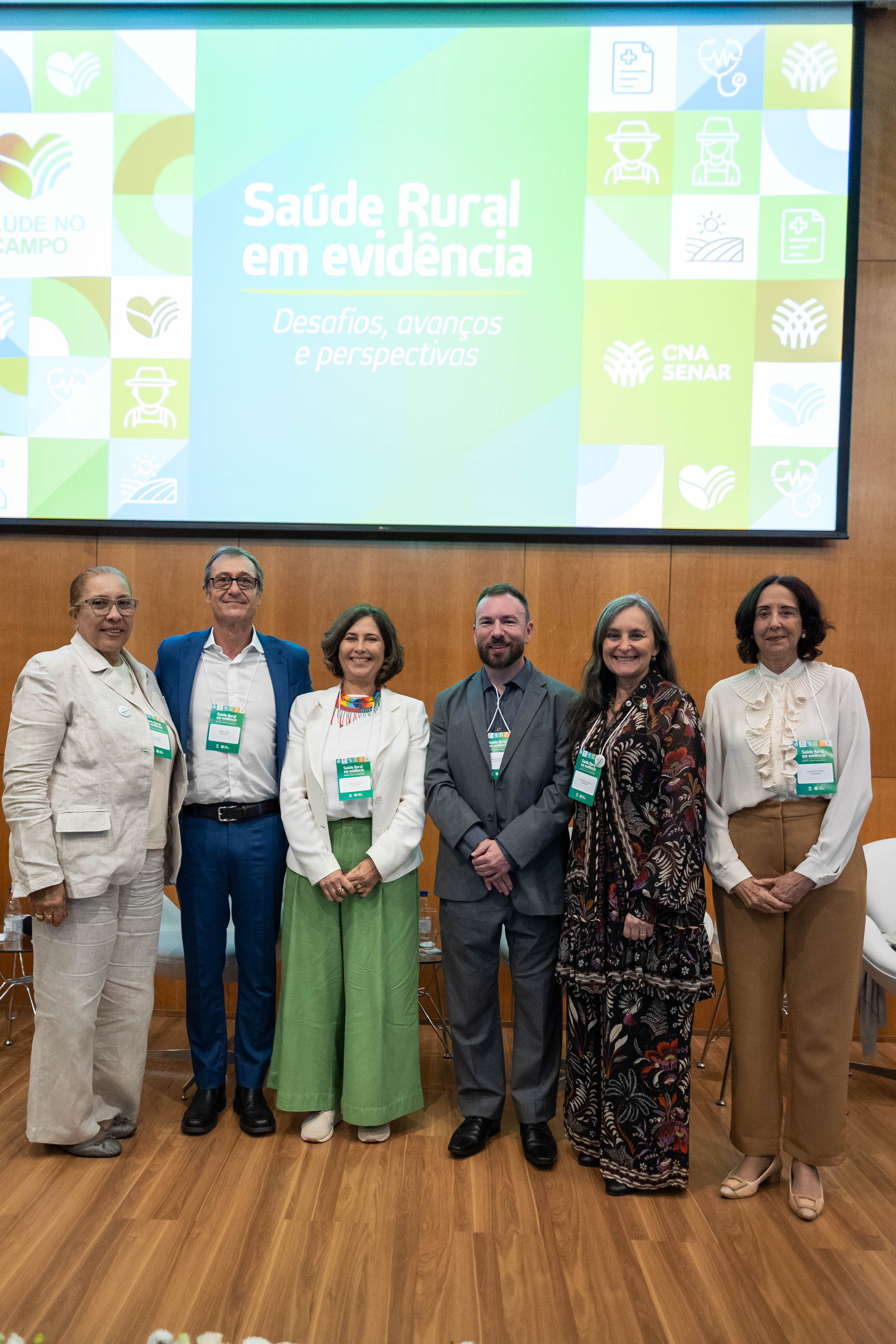 Seis palestrantes em pé no palco diante de um telão com os dizeres Saúde Rural em Evidência. A Dra. Dora Bernal está à esquerda e a Prof.ª Viviana Martinez-Bianchi é a segunda a partir da direita.